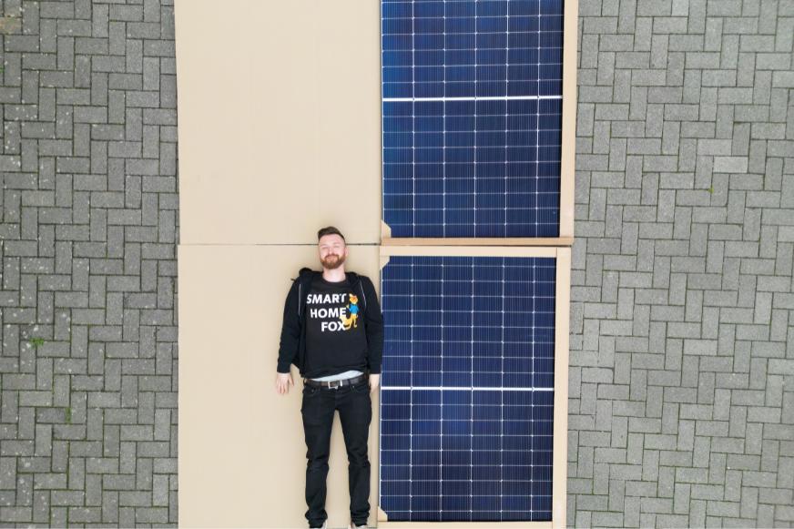 Der 180 cm große Smart-Home-Fox-Experte liegt neben den 2 Solarmodulen im direkten Größenvergleich.  